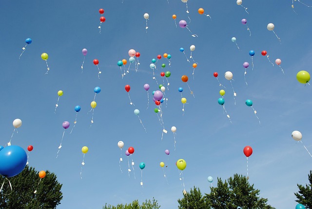 Picture of lots of balloons with message notes tied on them, floating in the sky.